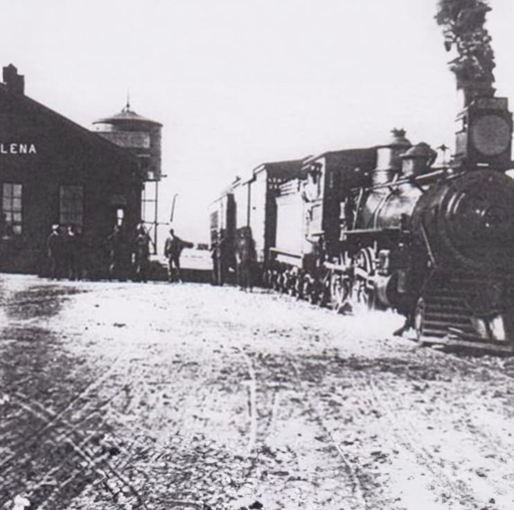 A train is coming down the tracks in front of a building.